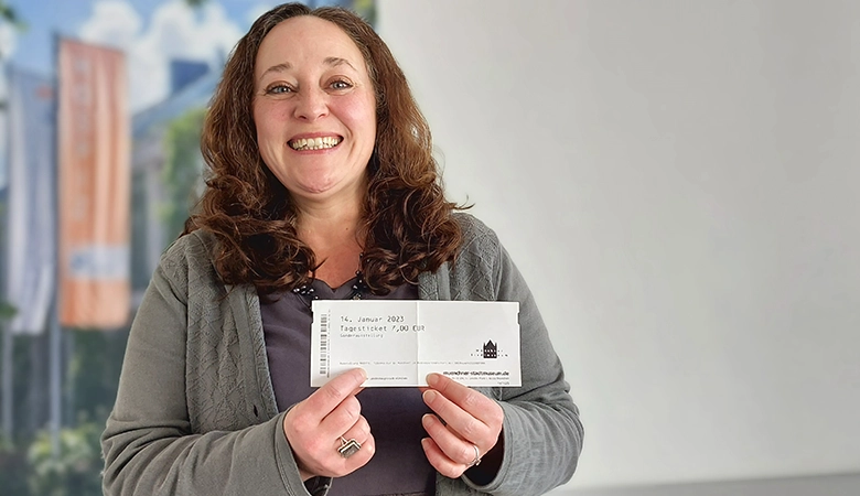 Julia Knoll zeigt lächelnd eine Eintrittskarte fürs Münchner Stadtmuseum. 