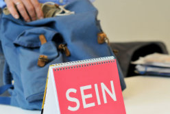 Dirk Addicks greift nach seinem Rucksack. Im Vordergrund ein Kalenderblatt mit der Aufschrift „SEIN“.
