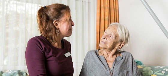 Porträt: Patientin und Pflegekraft sehen einander verschmitzt an.