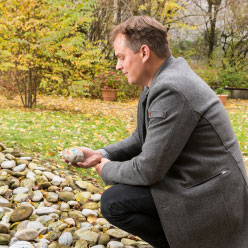 Ulrich Heller am „Fluss der Erinnerung“, eine Spur aus Kieselsteinen, die mit den Namen Verstorbener beschriftet sind.