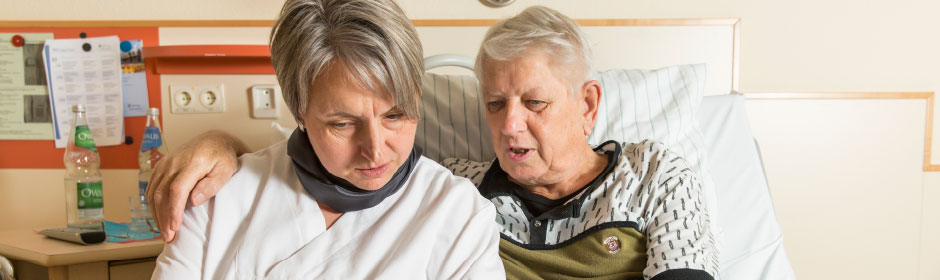 Patient und Pflegekraft in einem Krankenhauszimmer.