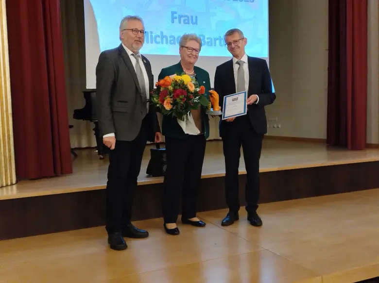 eine Frau mit Blumenstrauß und Preis steht zwischen zwei Männern