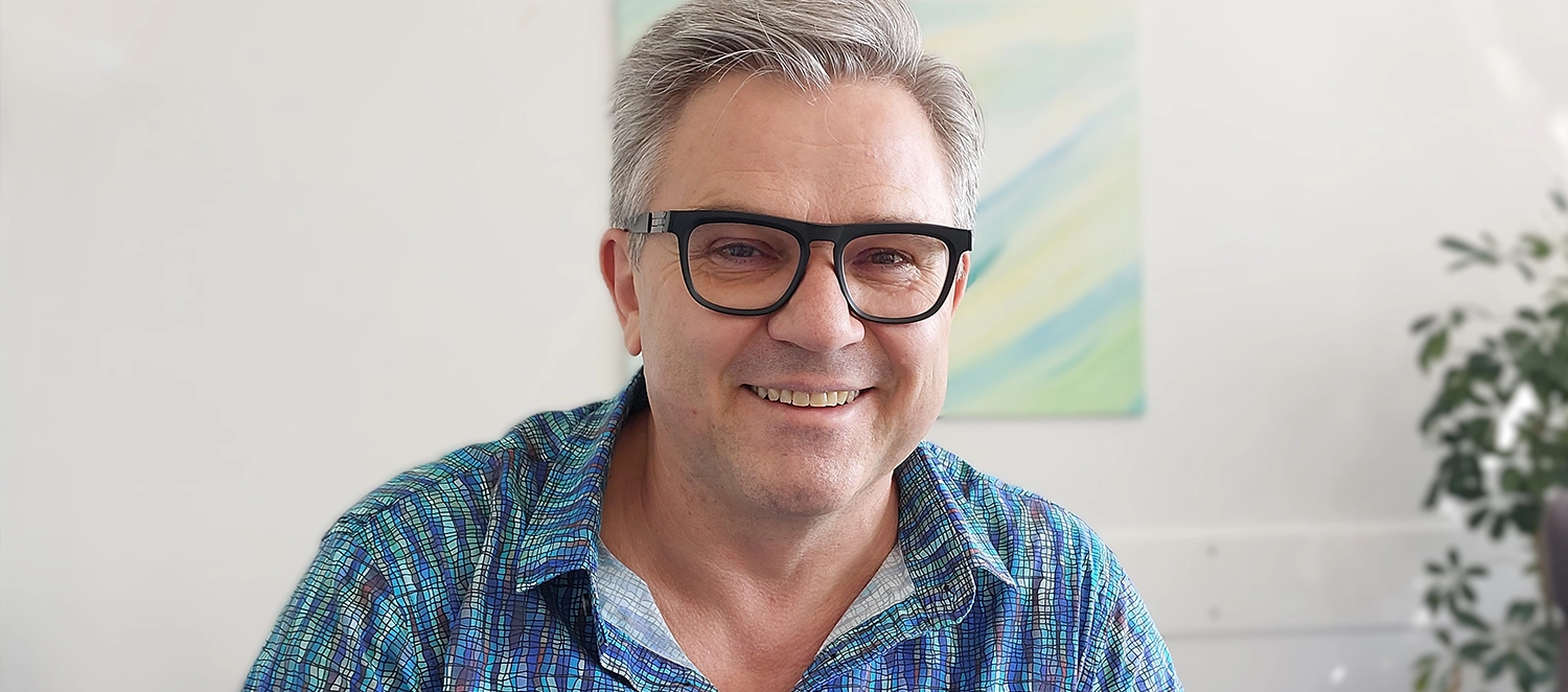 Porträt: Josef Hell. Er lächelt freundlich zugewandt. Er hat kurzes, graues Haar und trägt eine große schwarze Brille.