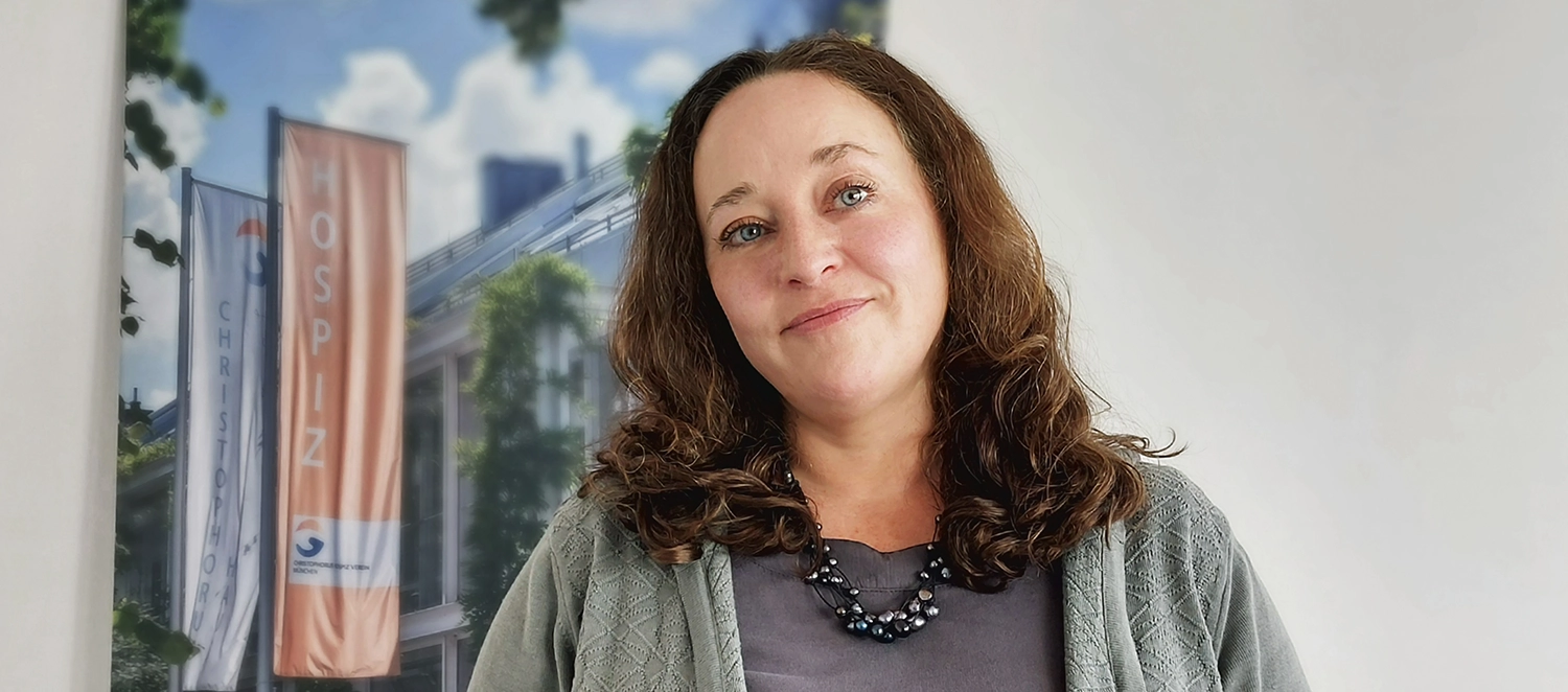 Julia Knoll, lange braune Haare, klares, ruhiges Gesicht, steht vor einem Poster eines Hospizvereins.