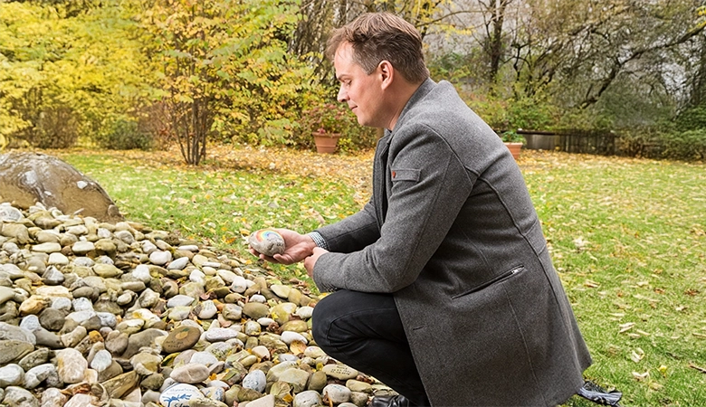 Ulrich Heller hat im Garten einen Stein in der Hand