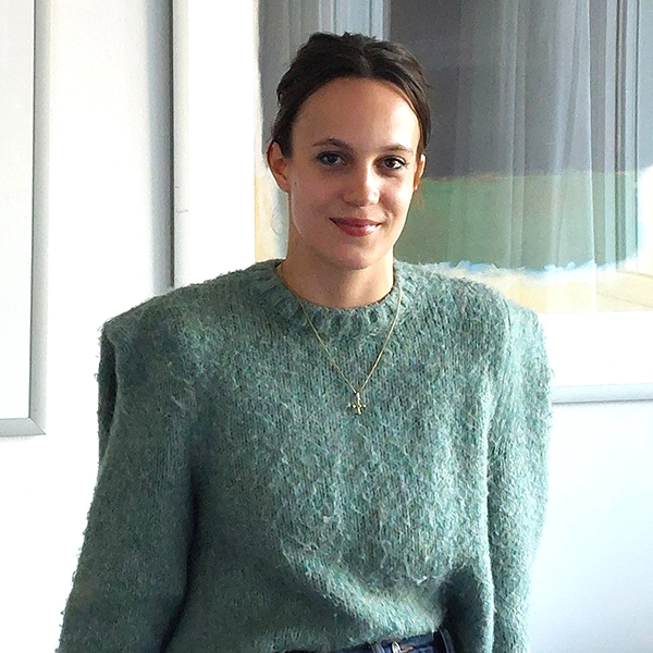 Anna, dunkle, hochgesteckte Haare, salbeigrüner Pulli, lächelt ruhig und freundlich in die Kamera. 