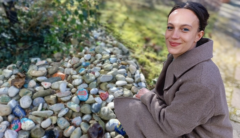 Anna vor einer Sammlung von Kieselsteinen, die Angehörige von Verstorbenen bemalt haben.
