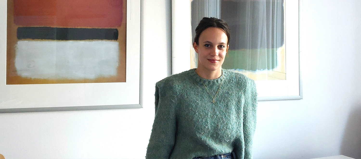 Anna, dunkle, hochgesteckte Haare, salbeigrüner Pulli, lächelt ruhig und freundlich in die Kamera.